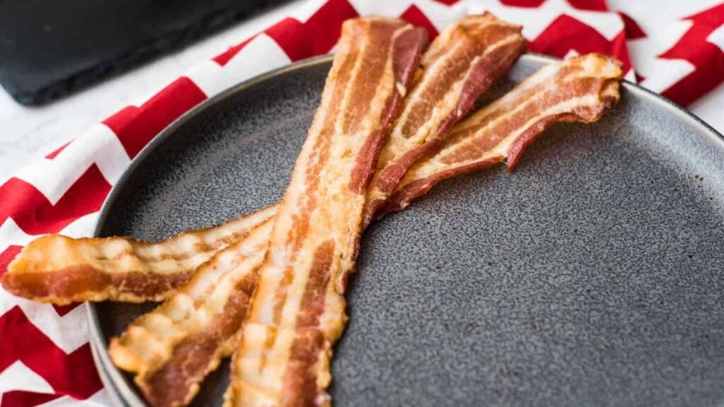 Three slices of cooked bacon on dark grey plate.