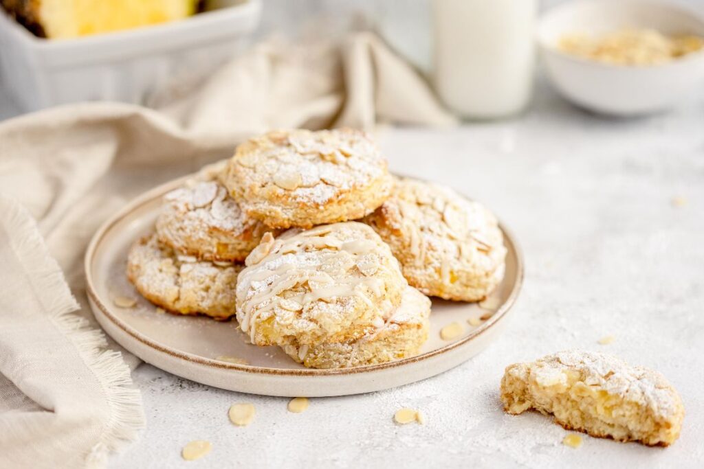 A plate of almond cookies dusted with powdered sugar, with a bitten cookie and milk in the background.