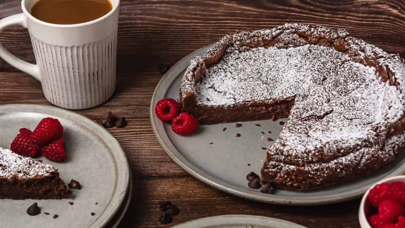 A chocolate cake dusted with powdered sugar, with raspberries and a cup of coffee on a wooden table.
