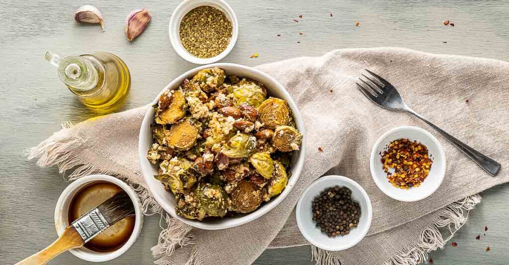 A bowl of roasted brussels sprouts with small jars of spices. 