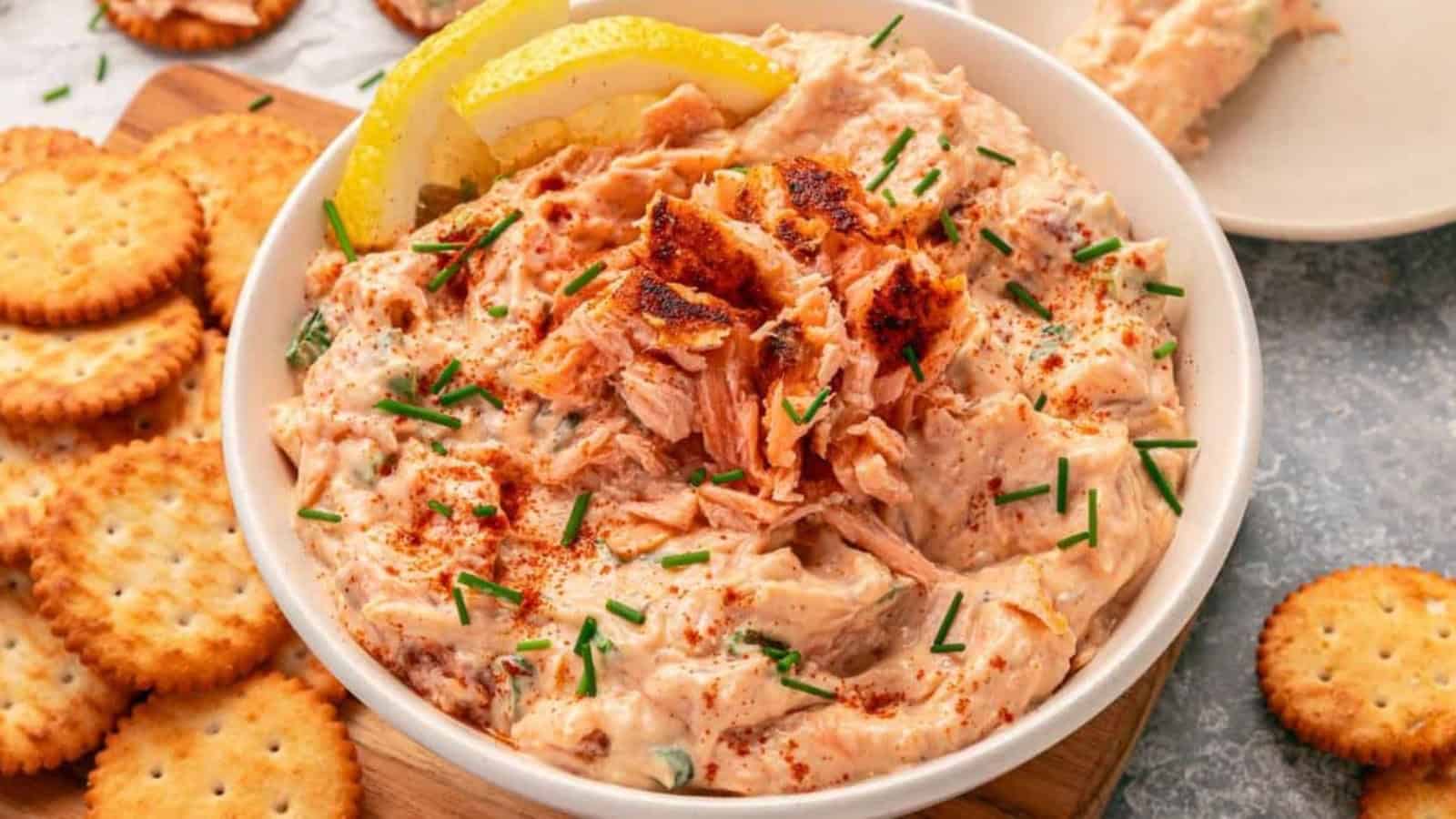 Creamy salmon dip garnished with chives and lemon slices, served with round crackers on the side.