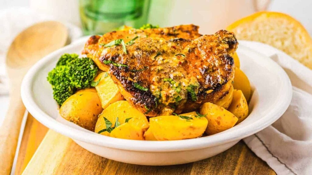 Grilled pork chops with roasted potatoes and broccoli served in a white bowl on a wooden surface.