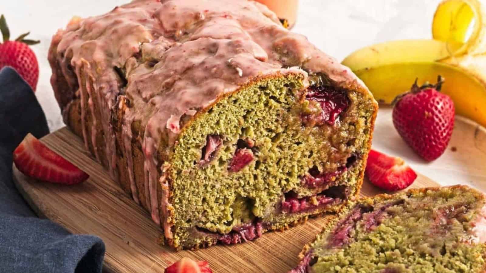 Sliced loaf of strawberry banana bread on a wooden board, surrounded by fresh strawberries and bananas.
