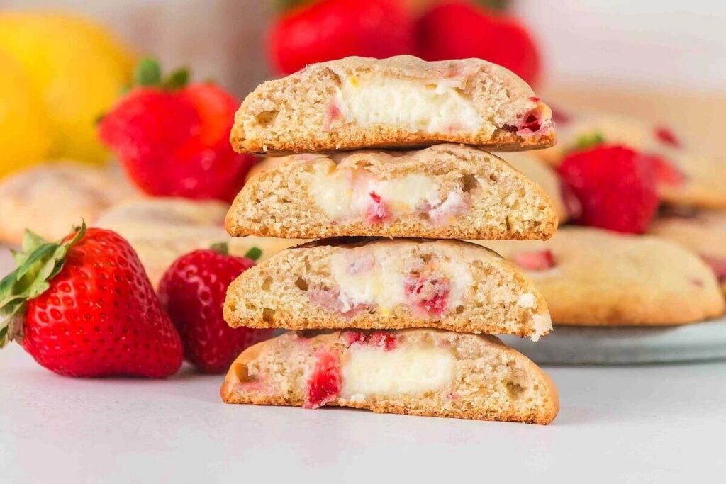 Four strawberry cheesecake cookies are stacked, revealing a luscious creamy filling.