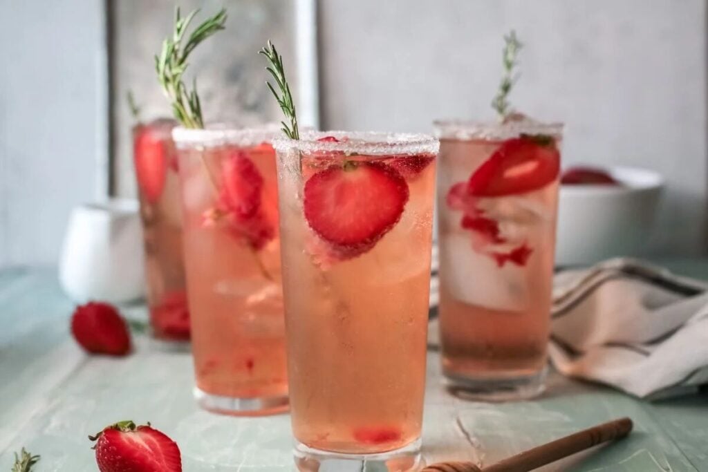 Two strawberry oatmeal bars are stacked on a wooden board, topped with whipped cream, with fresh strawberries and cinnamon sticks in the background.