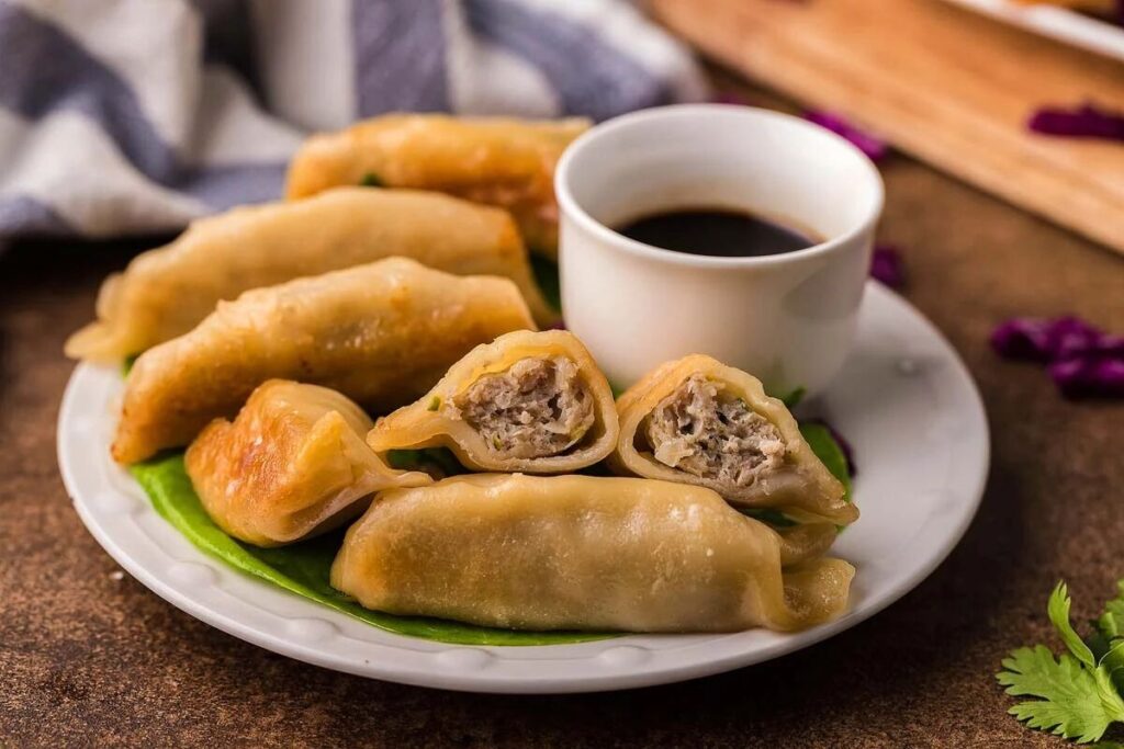 A plate of ground turkey potstickers, with one cut open to reveal the savory filling, sits invitingly next to a cup of soy sauce on a green leaf, elegantly placed on the table.