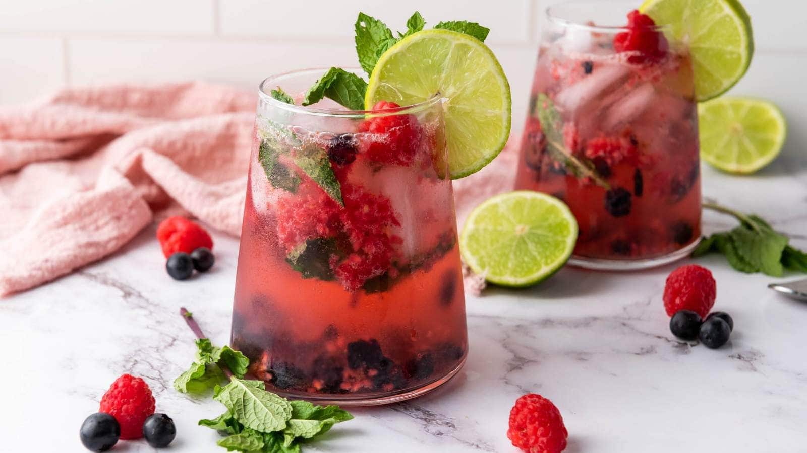 Two glasses of blueberry mocktail arranged on a marble surface with fresh mint and lime.