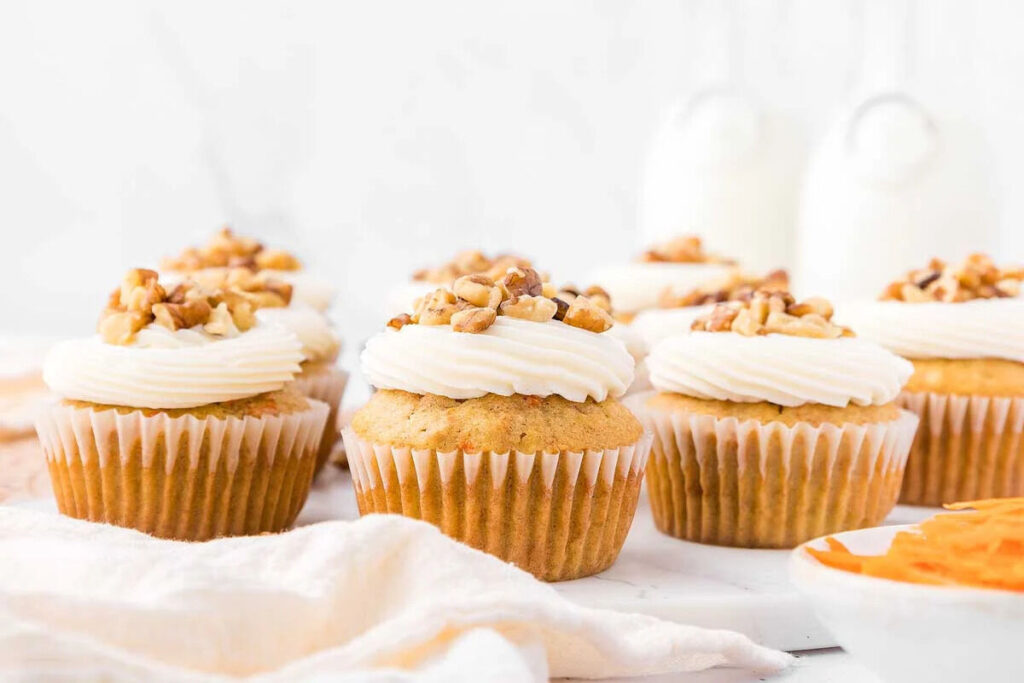 Delicious carrot cake cupcakes with icing and walnuts elegantly plated on white dish.