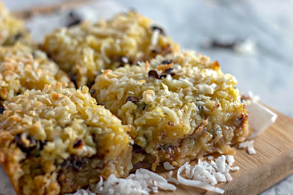 Gooey coconut bars on a wooden cutting board with coconut.