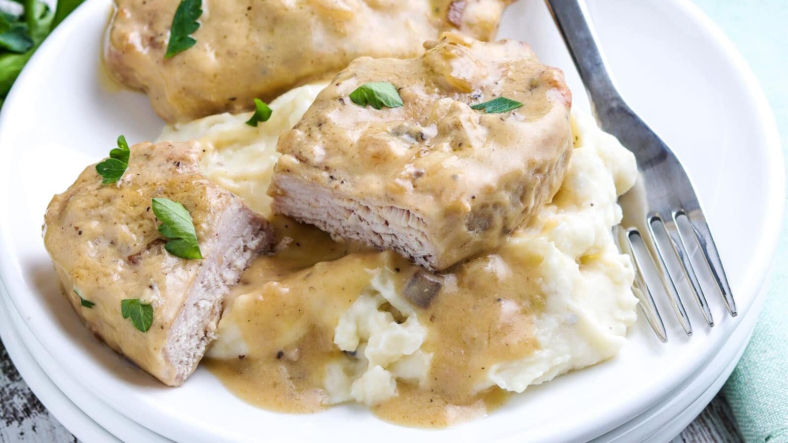 Slow Cooker Pork Chops on a plate covered with a creamy mushroom gravy and served on mashed potatoes.
