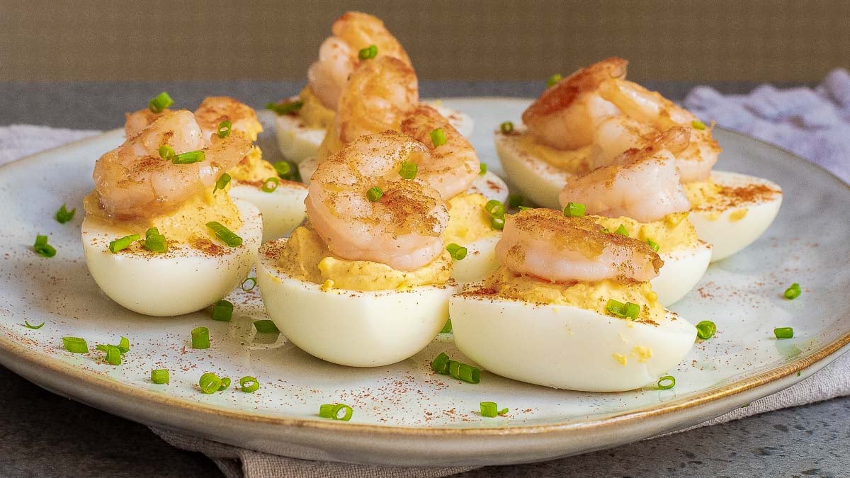 Deviled eggs topped with shrimp and garnished with chopped chives on a plate.