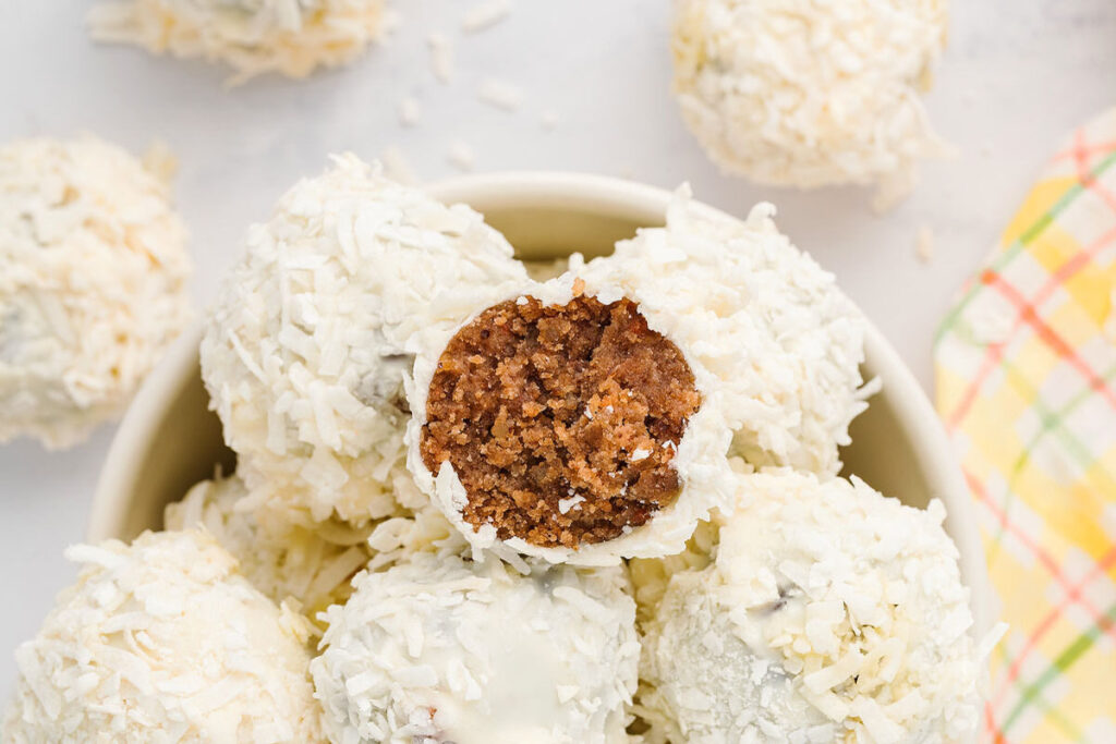 A bowl of carrot cake coconut truffles with a bite taken out of it.