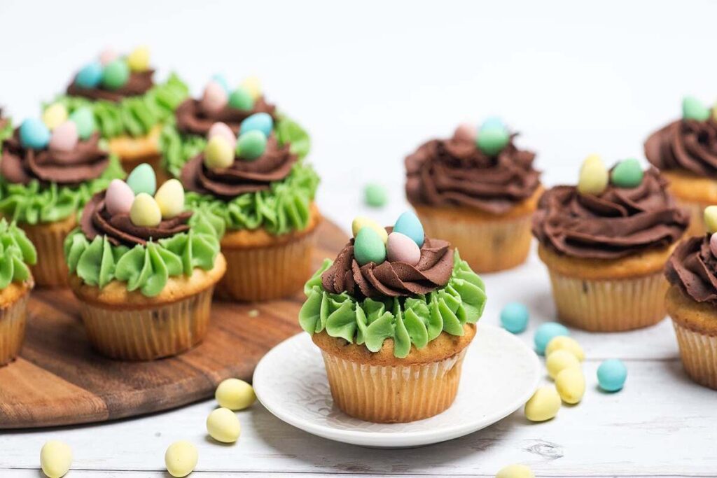A selection of Easter Mini Egg Nest Cupcakes adorned with green frosting and Cadbury mini eggs, displayed on a white wooden surface.