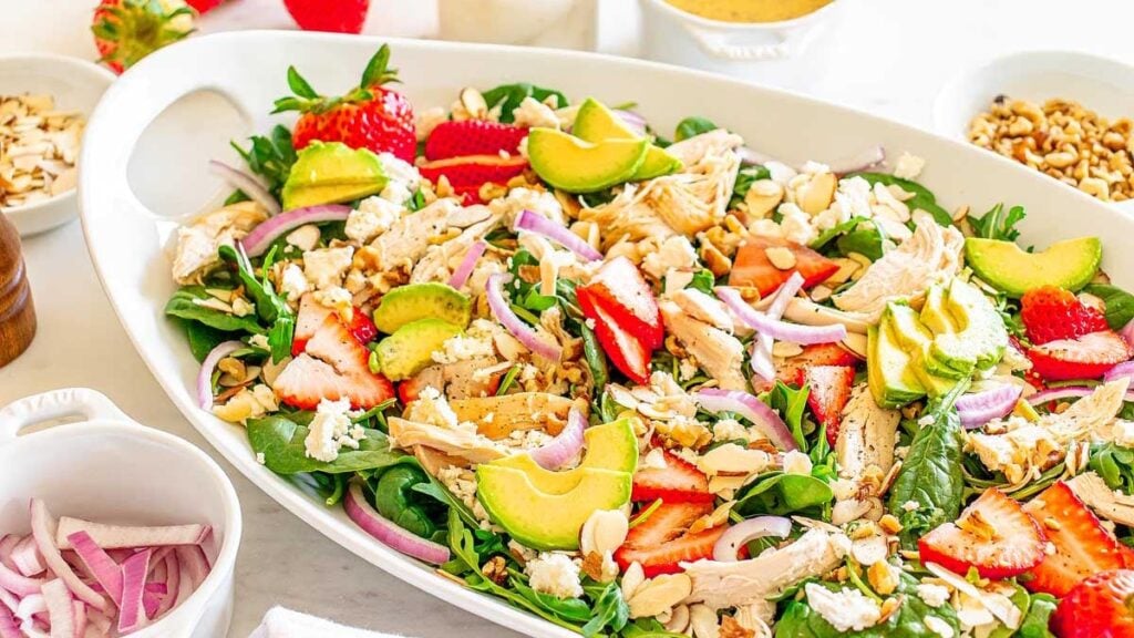 Strawberry fields salad with spinach, strawberries, avocado, chicken, feta, and nuts.