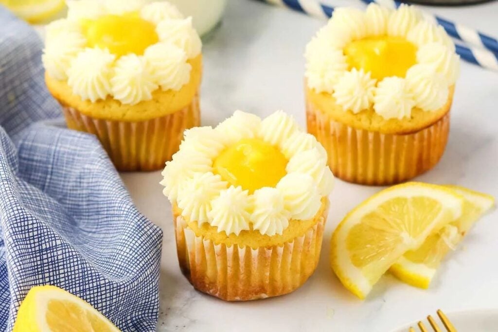 Lemon cupcakes with icing and lemon slices on a blue tablecloth.