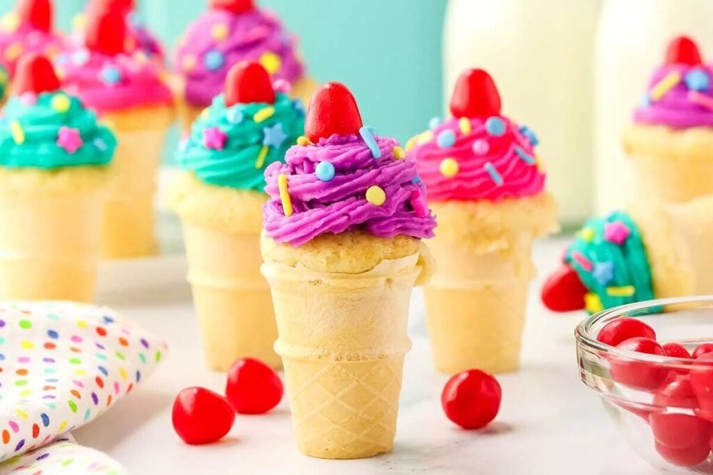 A group of cupcakes in mini ice cream cones with colorful frosting and candy.