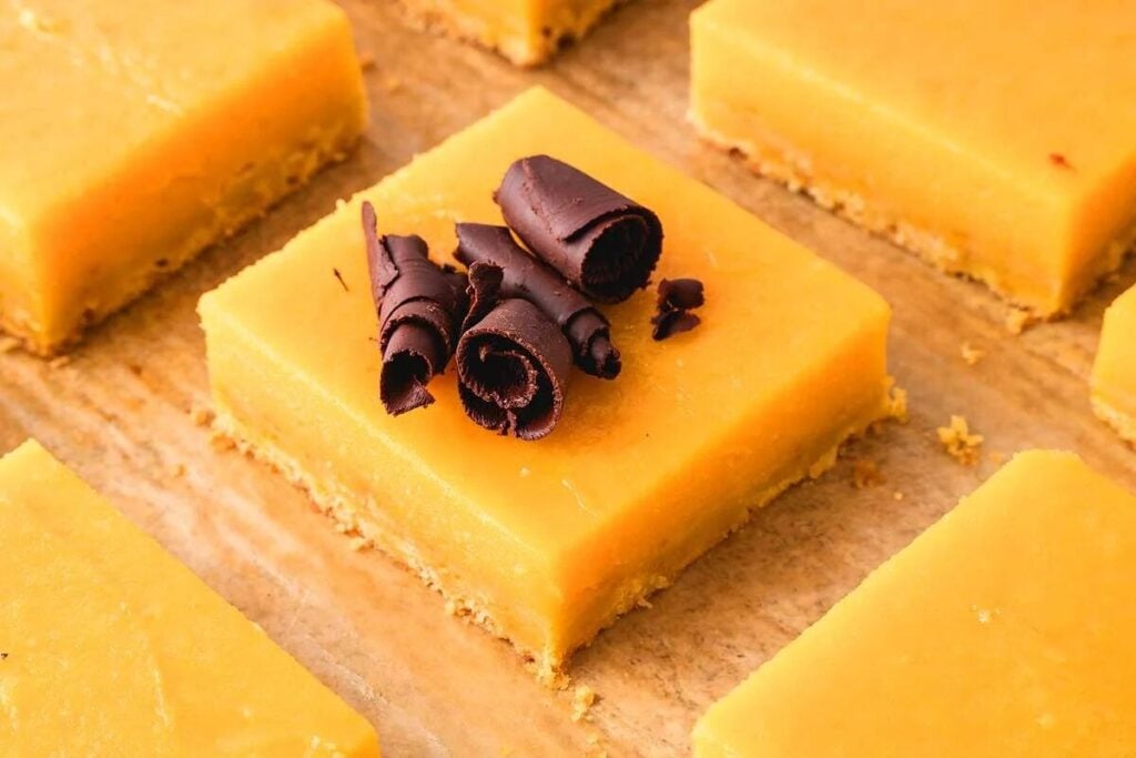 Orange bars topped with chocolate curls on a wooden surface.