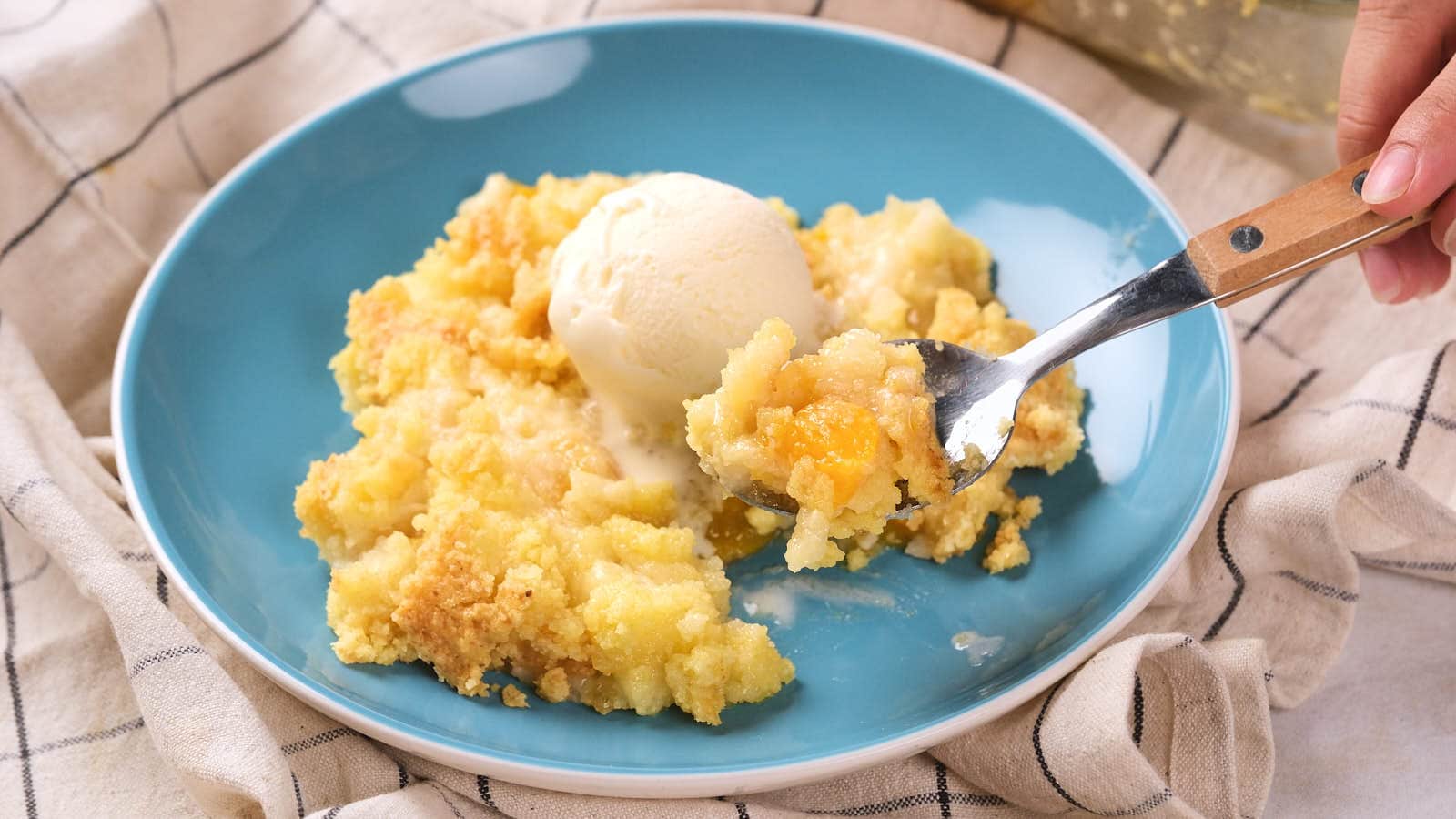 A plate of peach cobbler topped with a scoop of vanilla ice cream.
