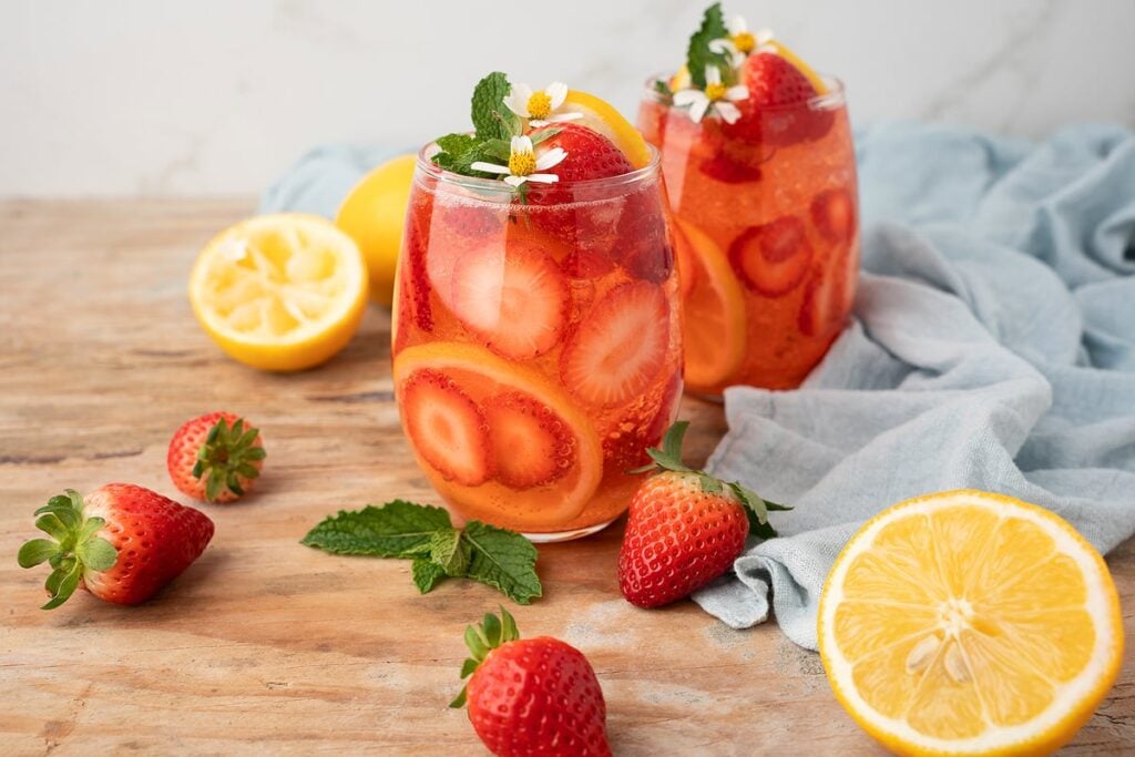 Two glasses of Strawberry lemonade on a table with strawberries and lemon halves.