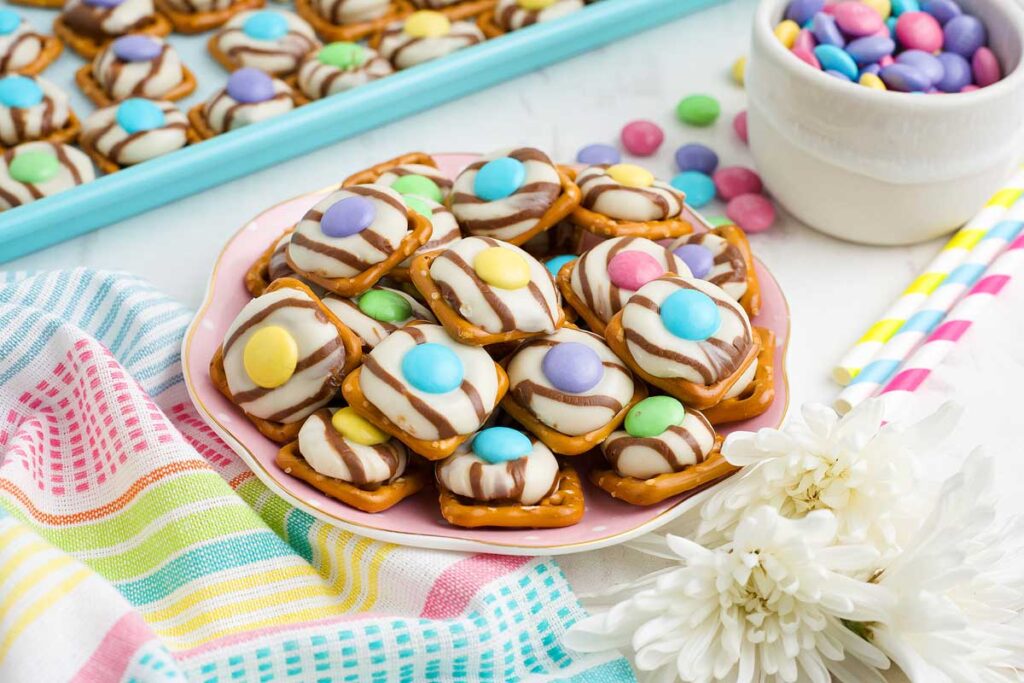A plate of Easter pretzel bites garnished with candy on a plate with flowers near the plate.
