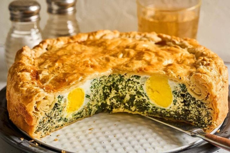 A savory Torta Pasqualina with golden crust, filled with spinach and whole boiled eggs, with a slice cut out.