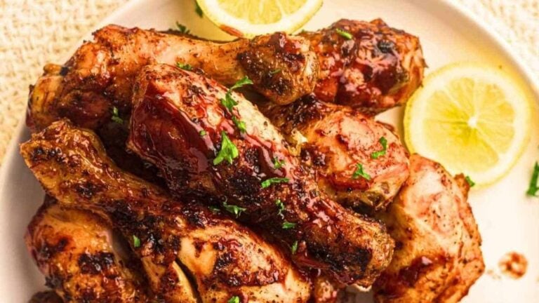 A plate of grilled chicken drumsticks garnished with chopped herbs, served with lemon slices.