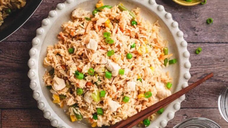 A plate of fried rice with vegetables, chicken pieces, and chopped green onions, with chopsticks on the side.