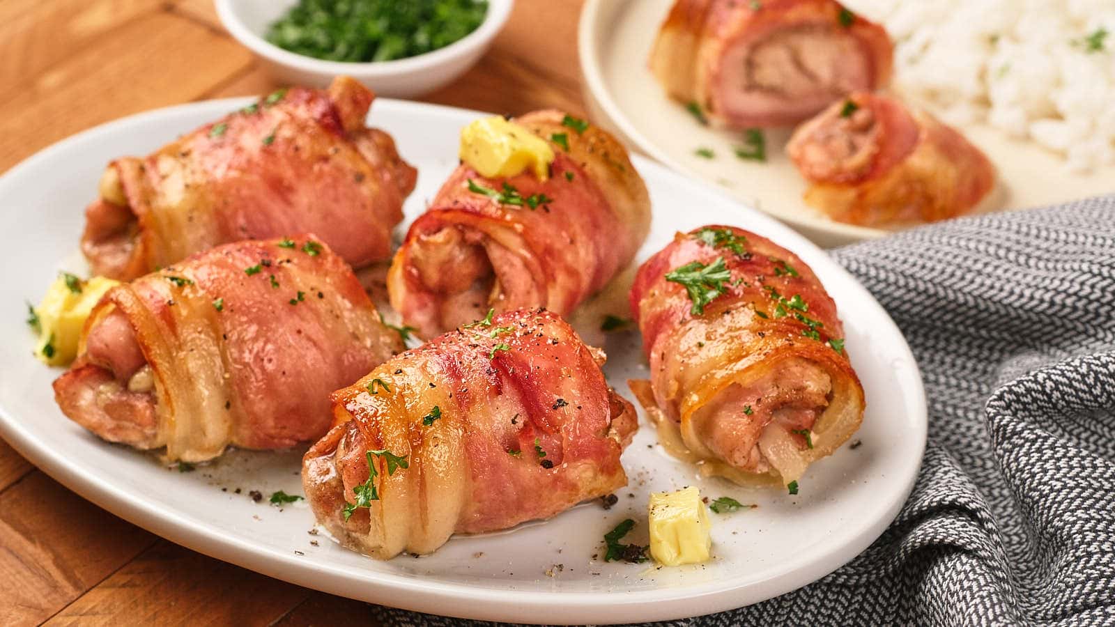 Four bacon-wrapped chicken thighs with parsley garnish on white plate.