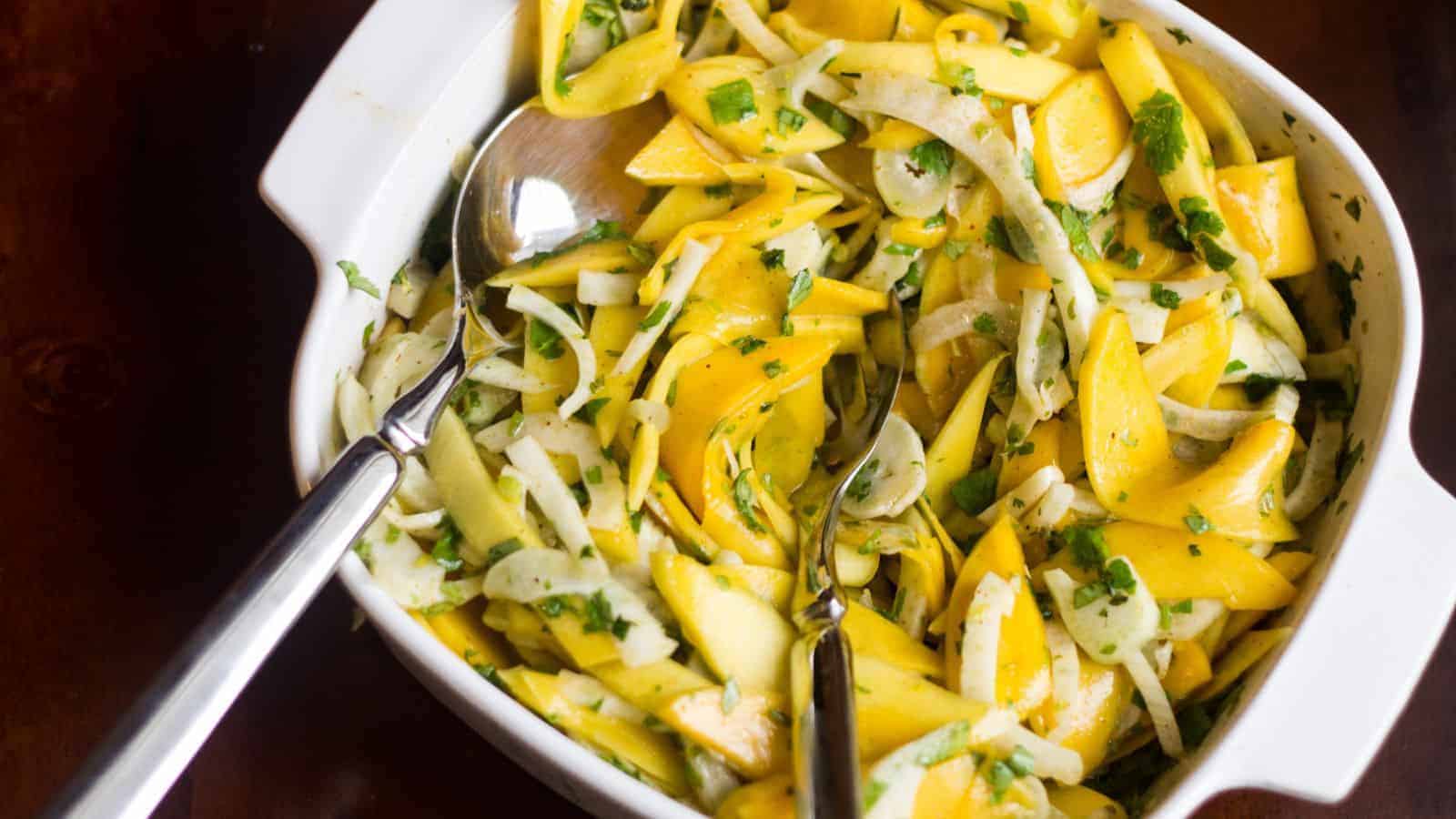 Fennel and mango slaw, featuring thinly sliced mango and shaved fennel, in a white serving dish.