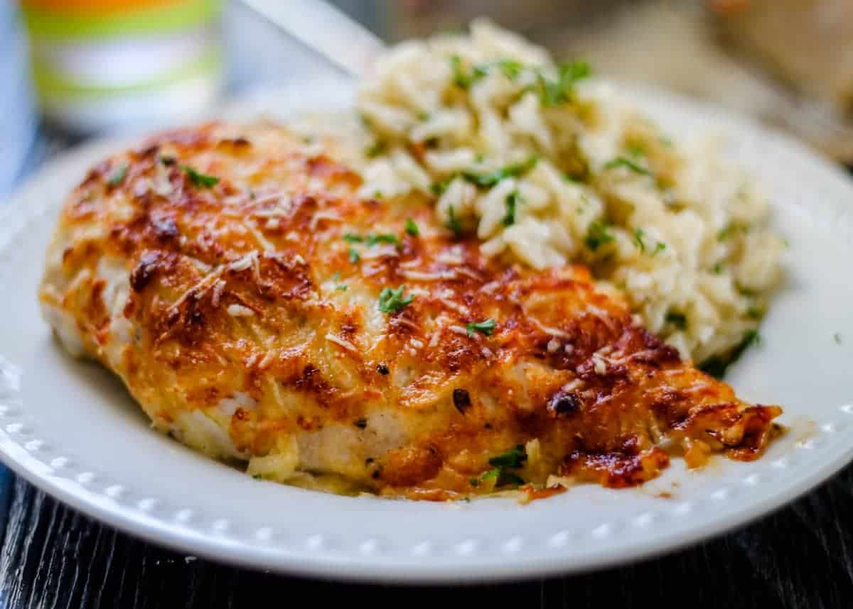 A plate with parmesan chicken on it with a side of rice.